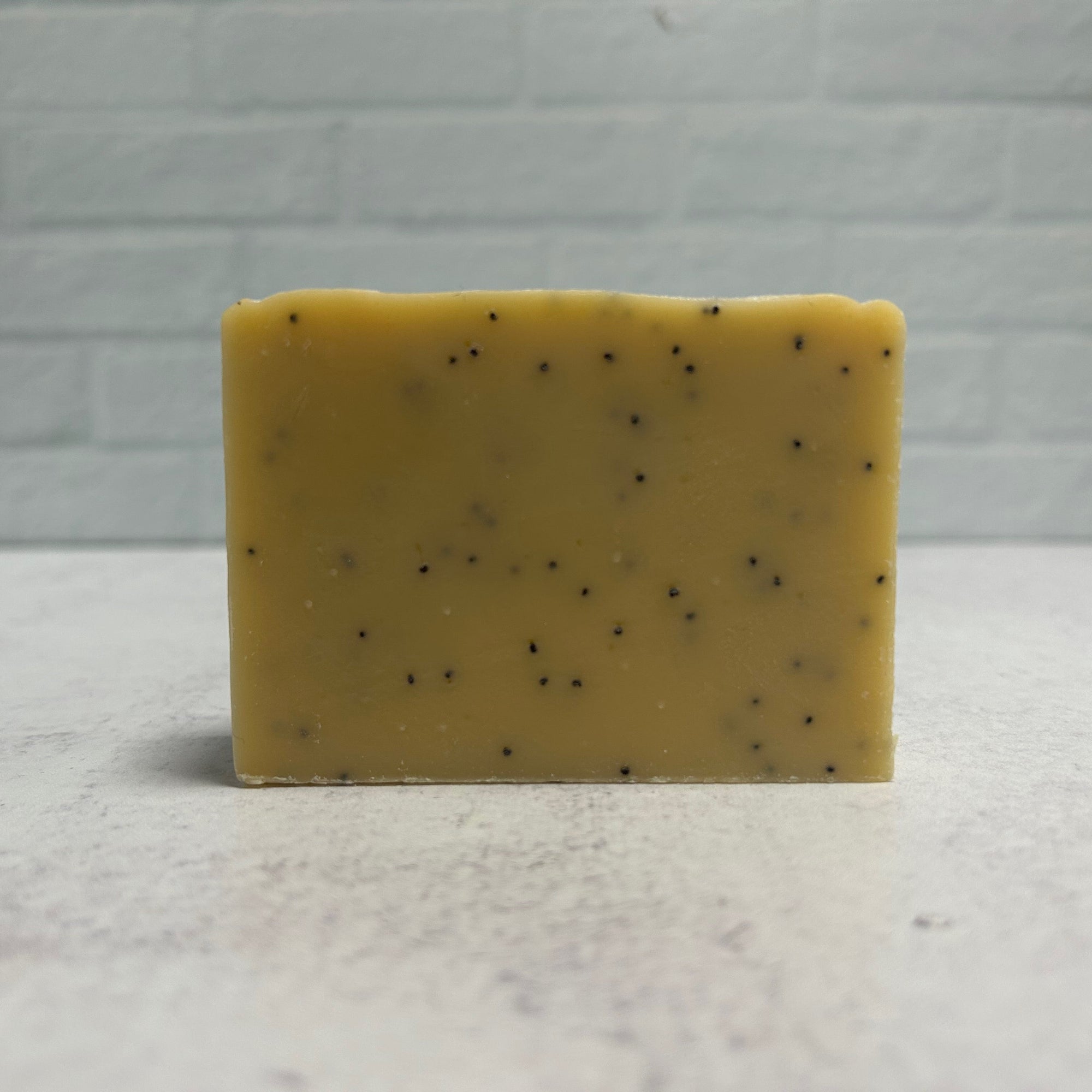 Yellow soap bar with black specks on a gray surface and background
