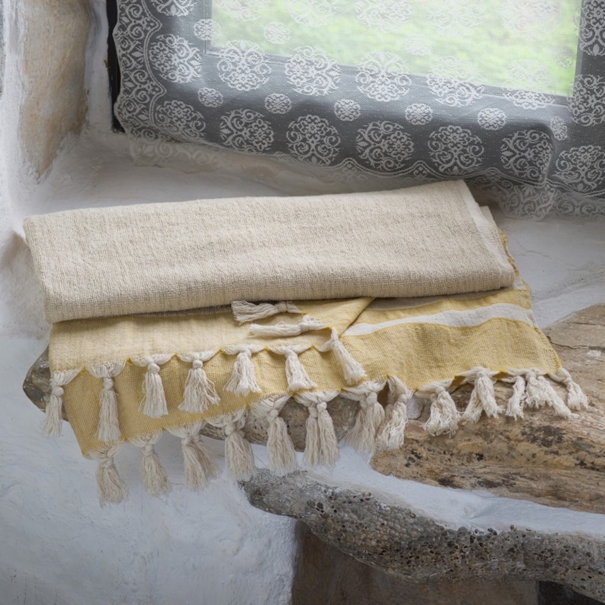 Yellow towel with tassels on a stone surface, with a patterned pillow in the background