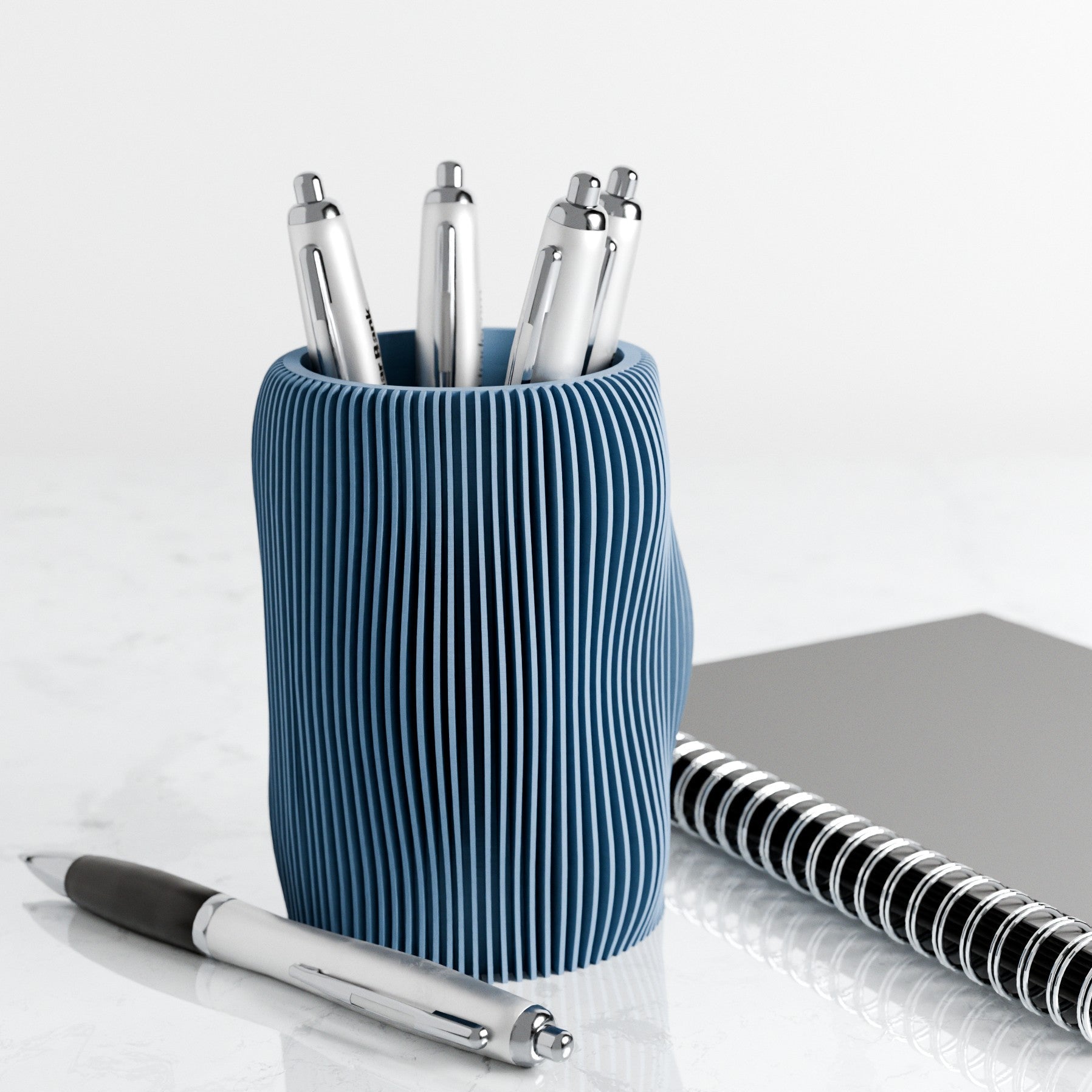 Blue textured pen holder with pens and a notebook on a white surface