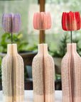 Three decorative paper vases with colorful tulip designed lids on a blurred natural background