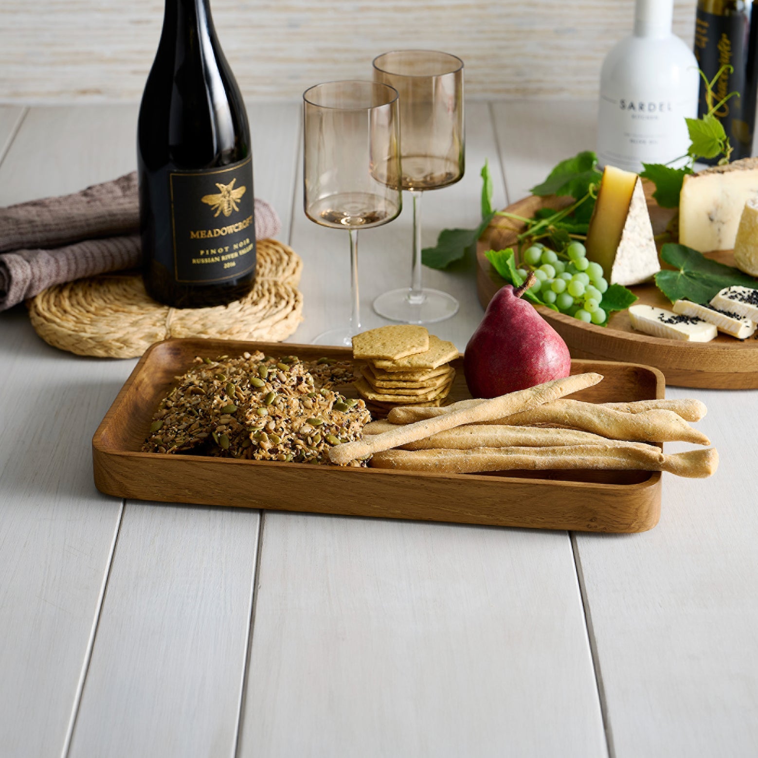 Wooden tray with appetizers on a table with wine and glasses.