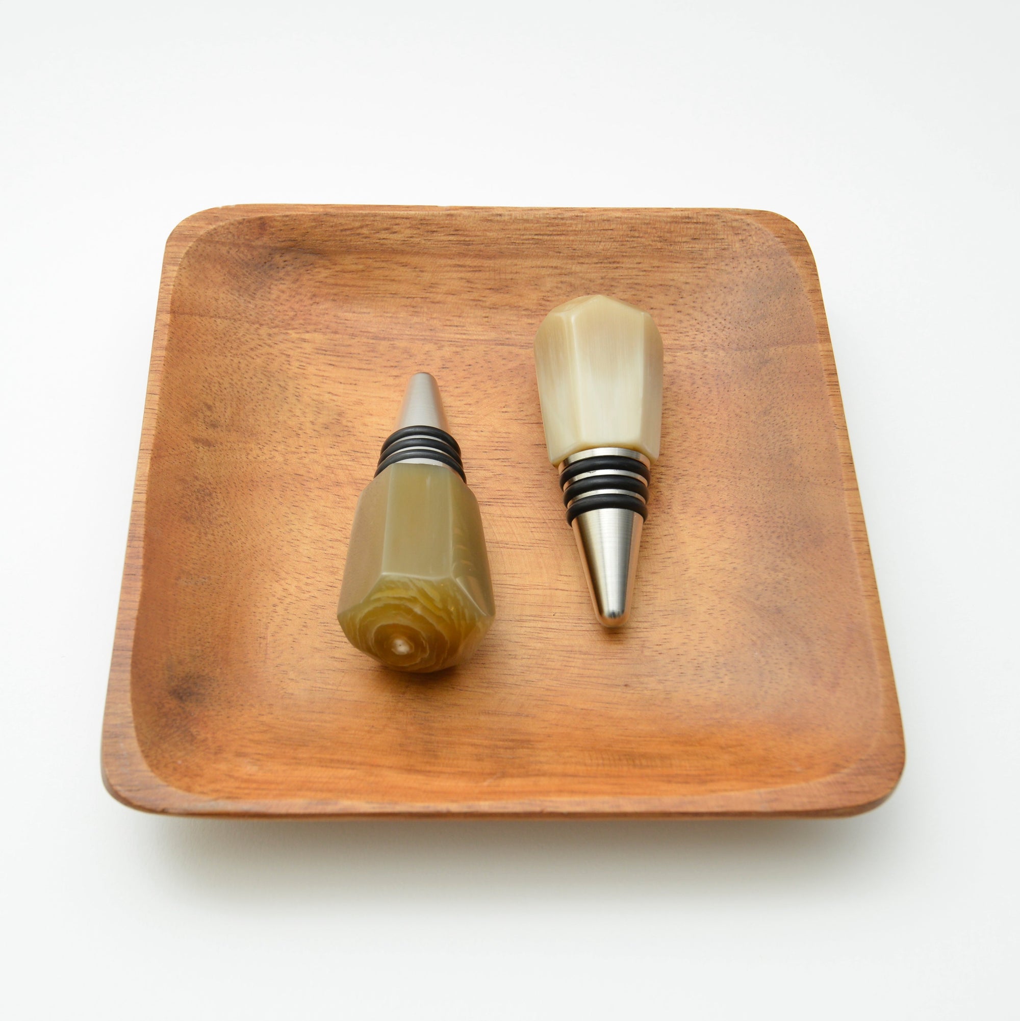 Two wine bottle stoppers on a wooden tray with a white background