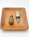Two wine bottle stoppers on a wooden tray with a white background