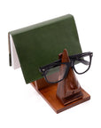 Green leather wallet and black glasses on a wooden stand against a white background