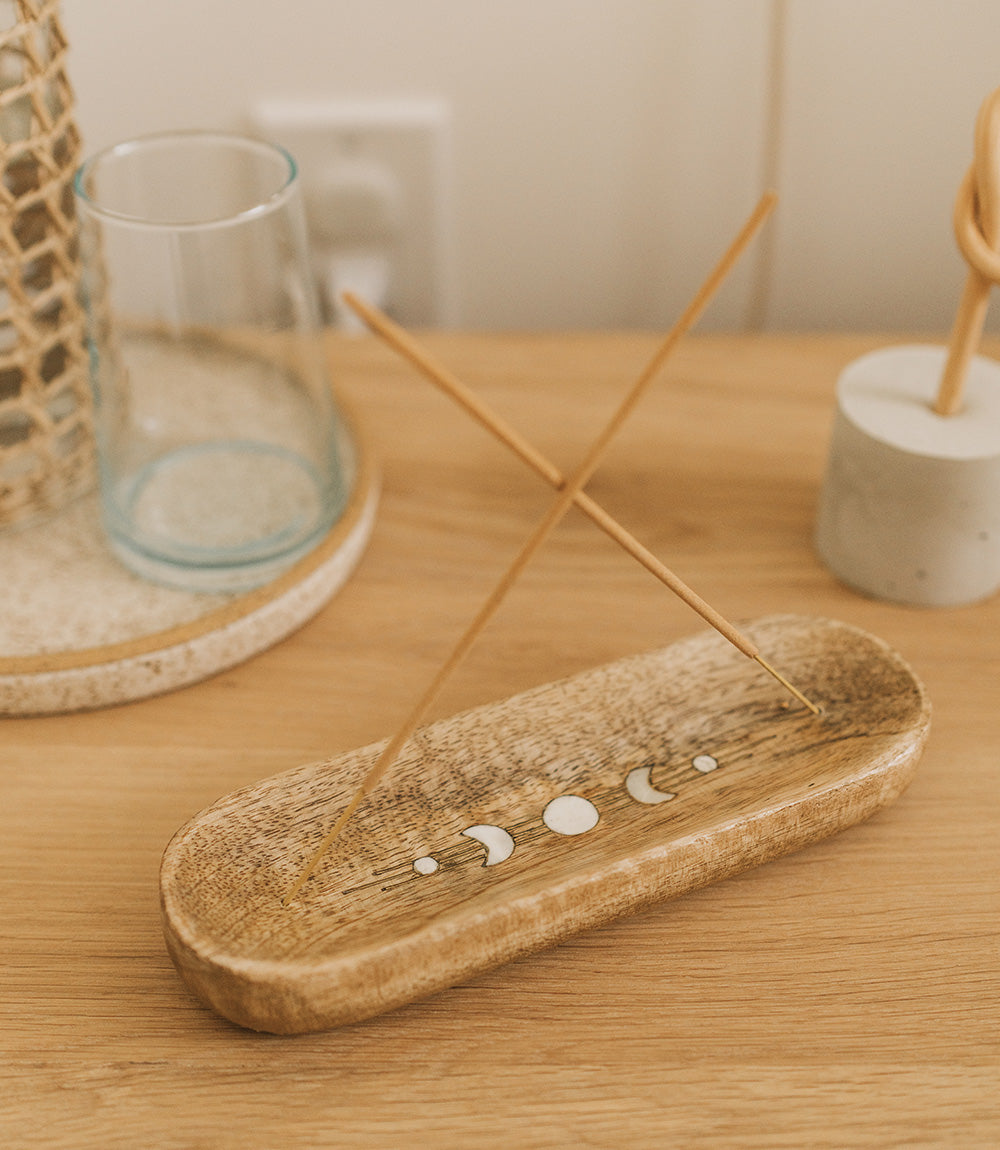 Incense sticks on a wooden holder with a decorative moon phase design on a wooden surface.