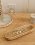 Incense sticks on a wooden holder with a decorative moon phase design on a wooden surface.