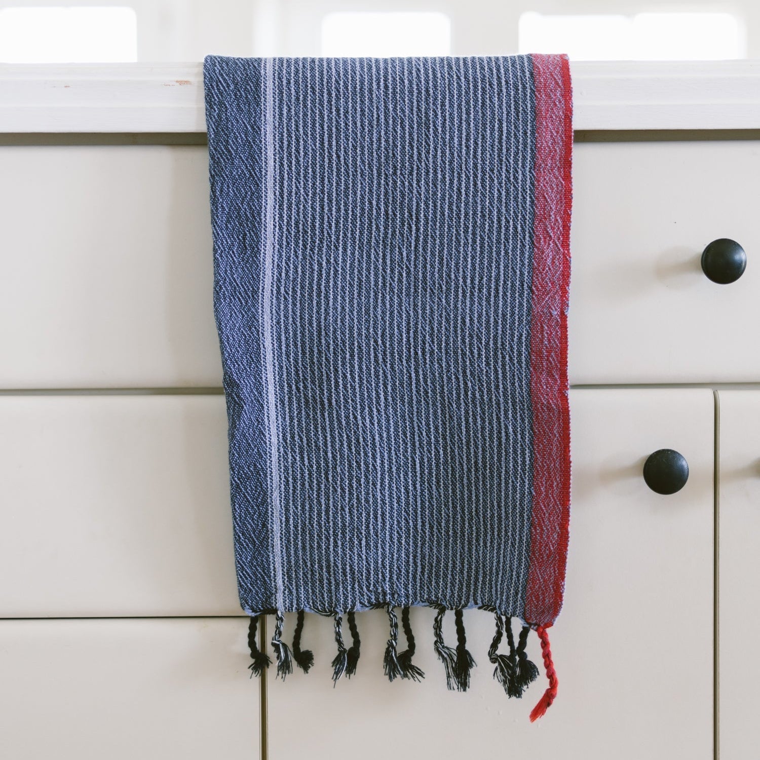 Blue and red striped towel hanging on a white cabinet with black knobs.