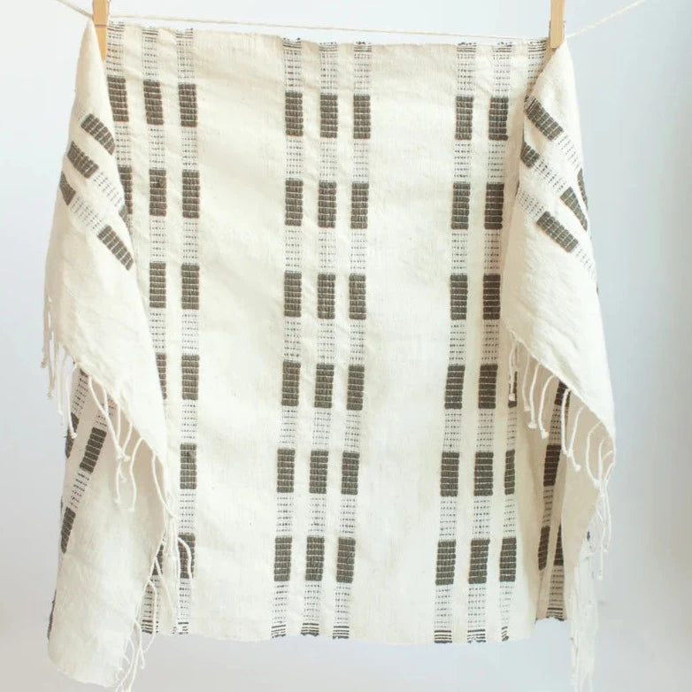 Gray and beige hand towel with fringe hanging from clippers on a white background