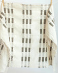 Gray and beige hand towel with fringe hanging from clippers on a white background