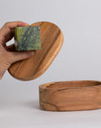 Wooden box with a lid being held open by a hand, revealing a stone inside.