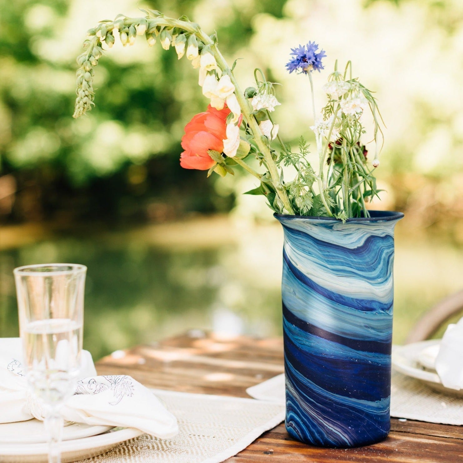 Blue glass vase with flowers on a table outdoors