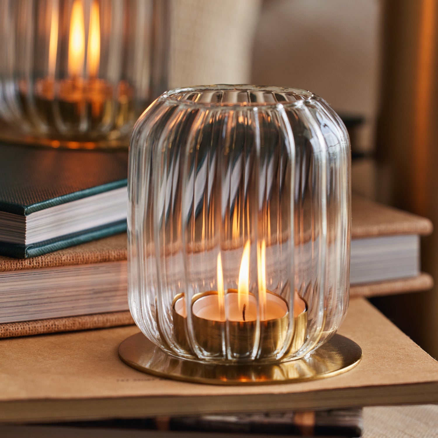 Clear glass candle holder with a lit candle on top of books
