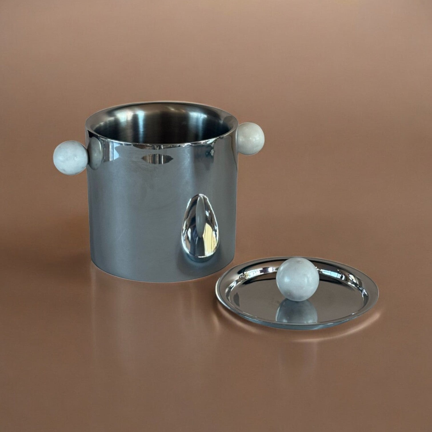Silver ice bucket with marble handles and base on a brown background