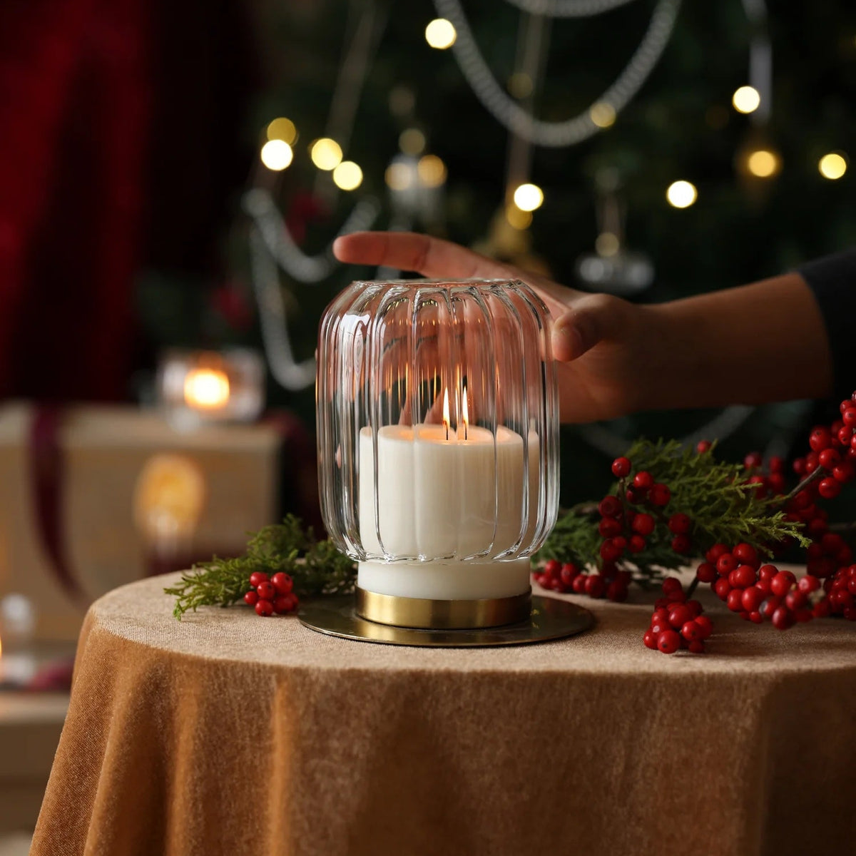 Candle in a glass lantern on a table with a decorated Christmas tree in the background