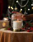 Candle in a glass lantern on a table with a decorated Christmas tree in the background