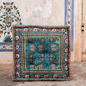 A square floor cushion with a floral hand-pressed design in multicolor on a cotton surface.