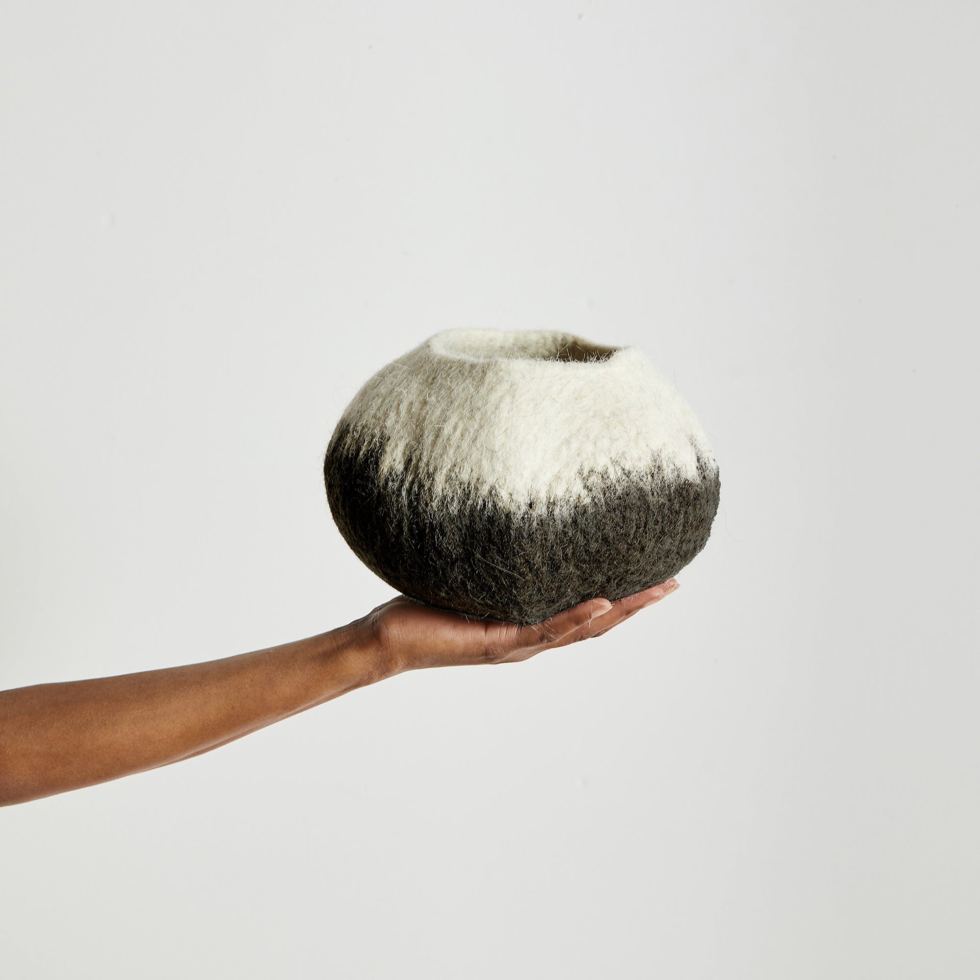Hand holding a black and white decorative wool bowl against a plain background