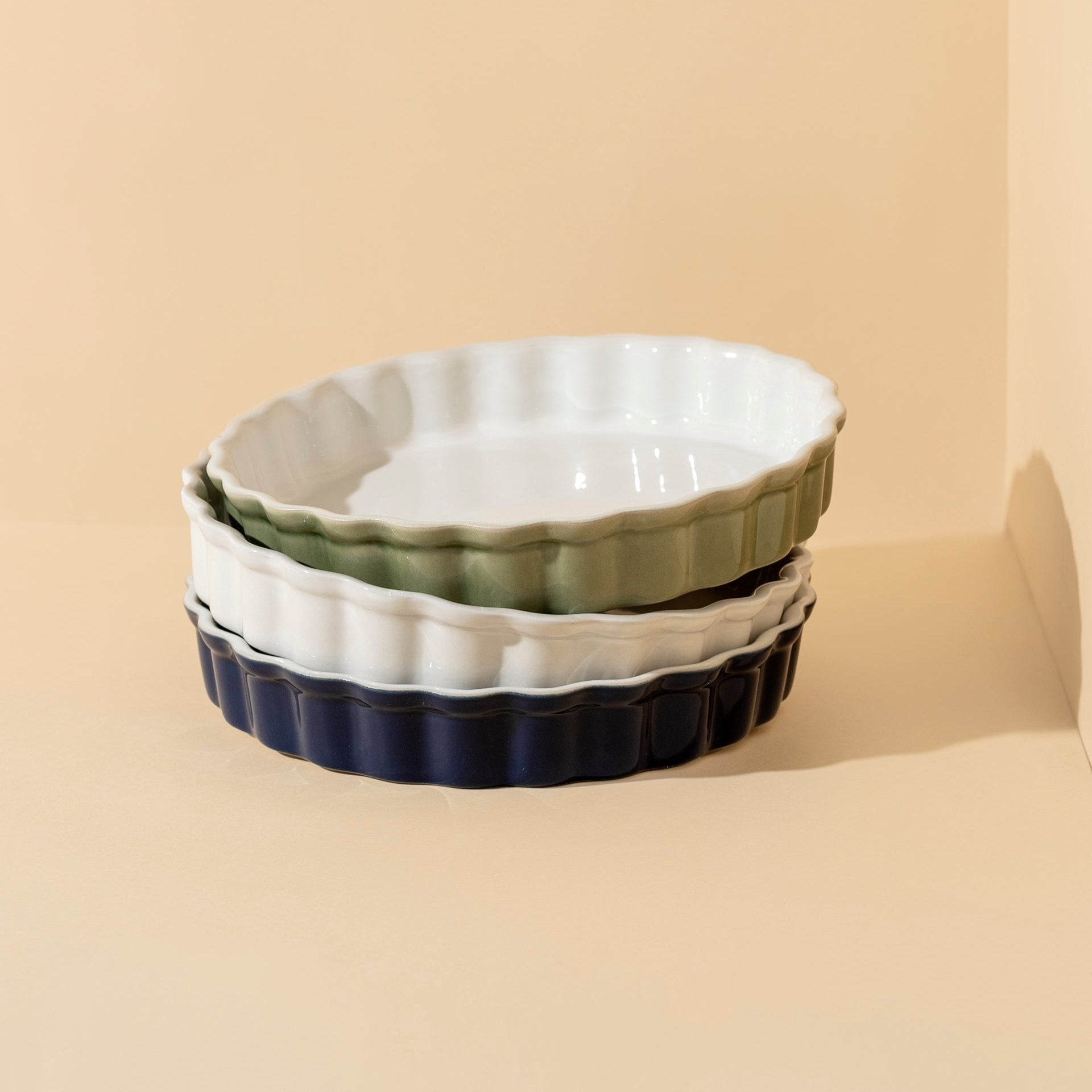 Set of three ceramic baking dishes in white, green, and navy on a beige background