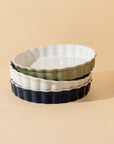 Set of three ceramic baking dishes in white, green, and navy on a beige background