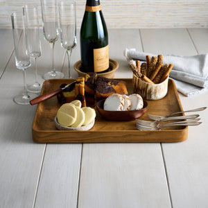 Wooden tray with cheese, crackers, and a bottle of wine on a light wooden surface