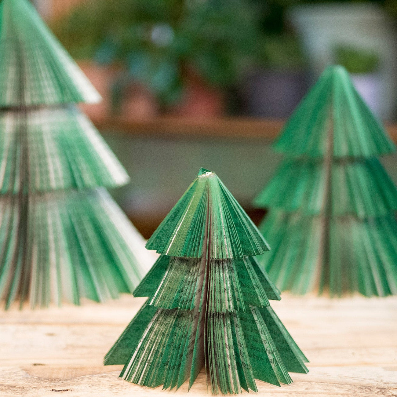 Three green paper Christmas trees on a wooden surface with a blurred background