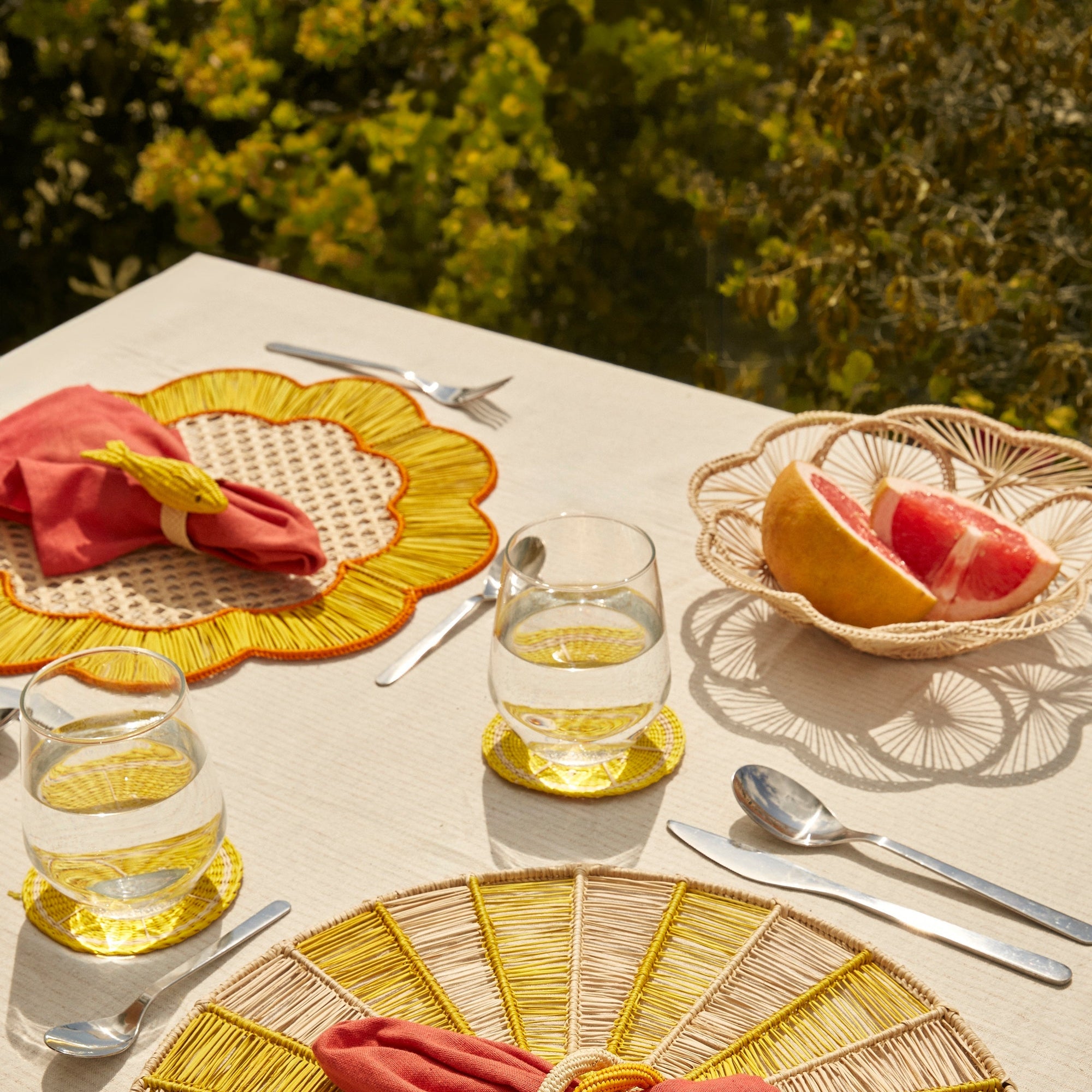 Table setting with woven baskets, placemats, red napkins, and glasses on a natural outdoor background.