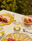 Table setting with woven baskets, placemats, red napkins, and glasses on a natural outdoor background.