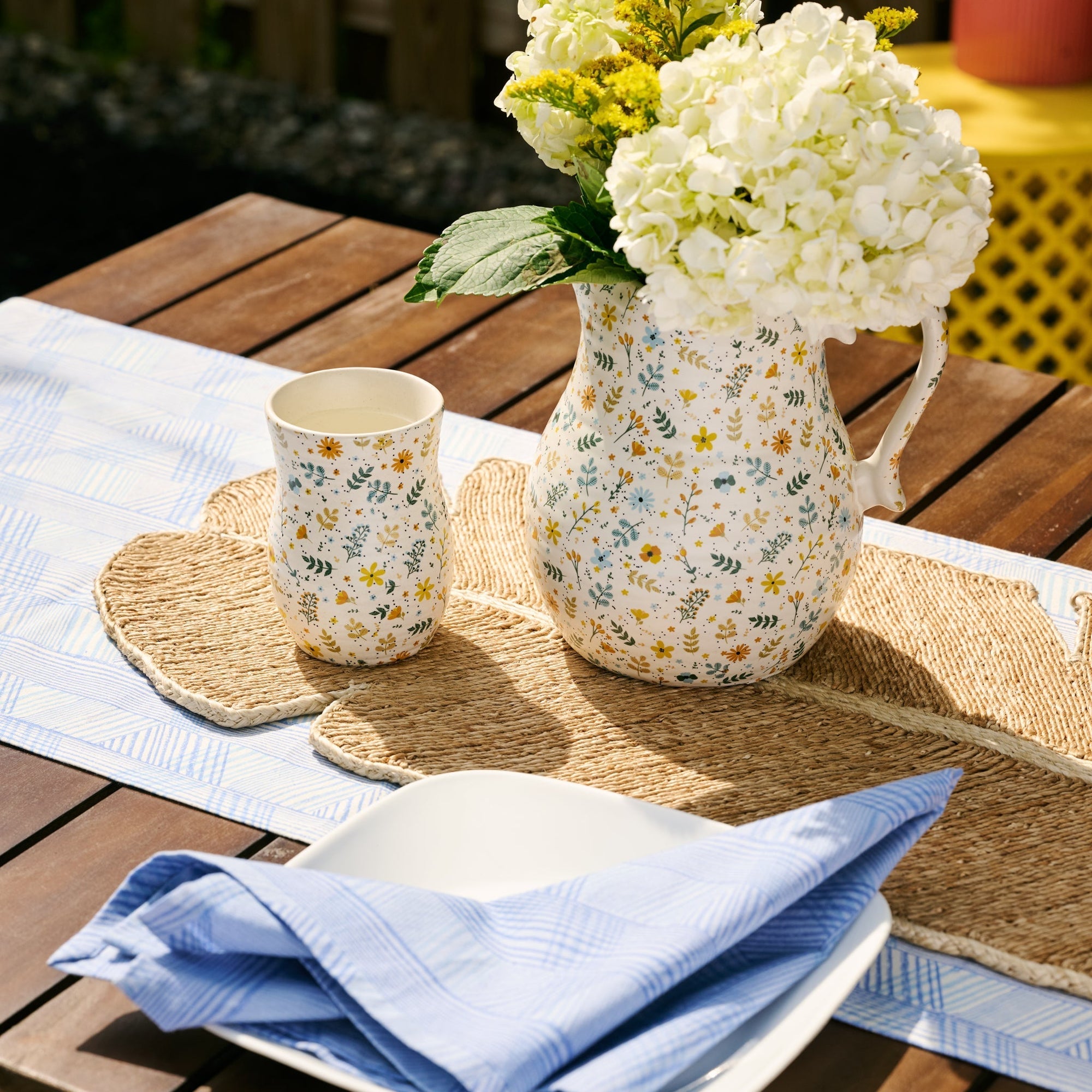 Decorative floral pitcher and mug on a wooden table with a blue napkin