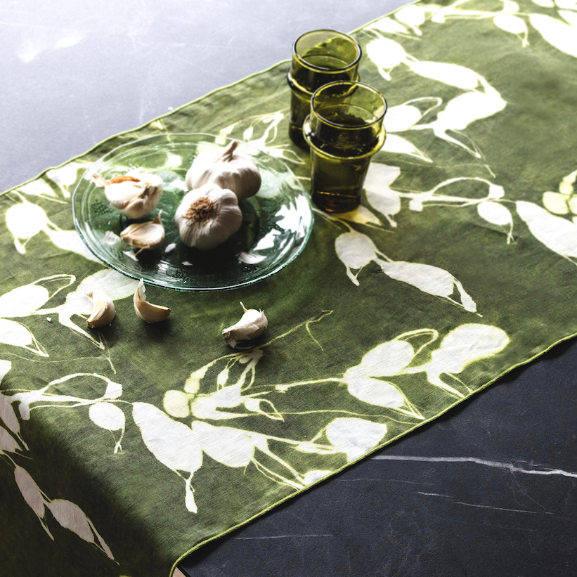 Table setting with garlic bulbs and olive oil glasses on a green floral table runner