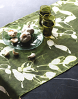 Table setting with garlic bulbs and olive oil glasses on a green floral table runner