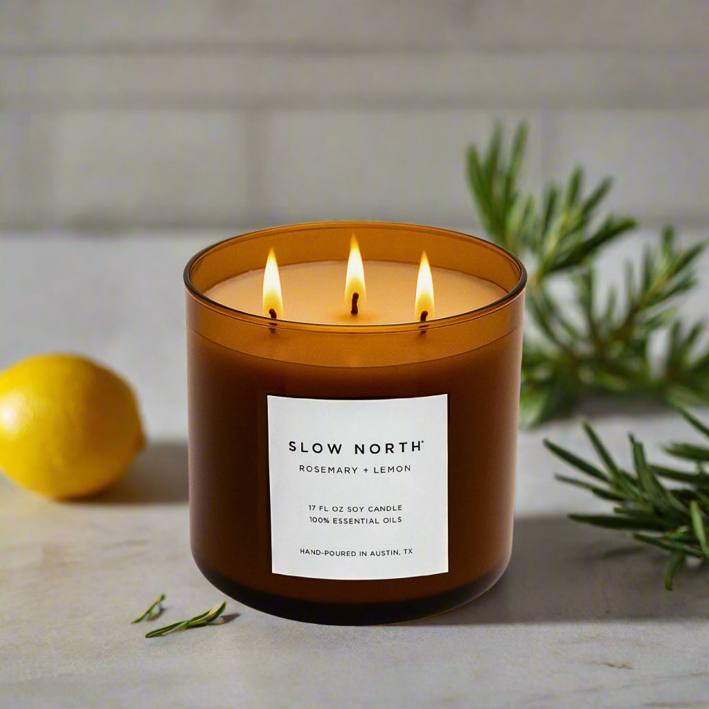 Candle with 'Slow North' label on a surface with a lemon and greenery