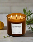 Candle with 'Slow North' label on a surface with a lemon and greenery