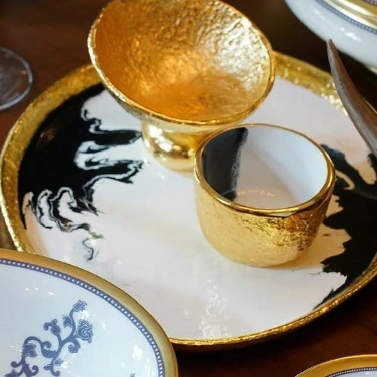 Gold-rimmed ceramic cups on a decorative plate with artistic design