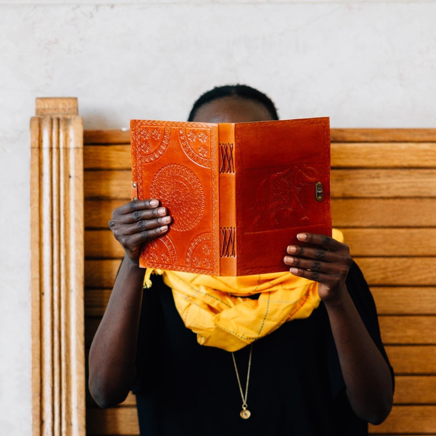 Person holding a red journal in front of their face while sitting on a wooden chair