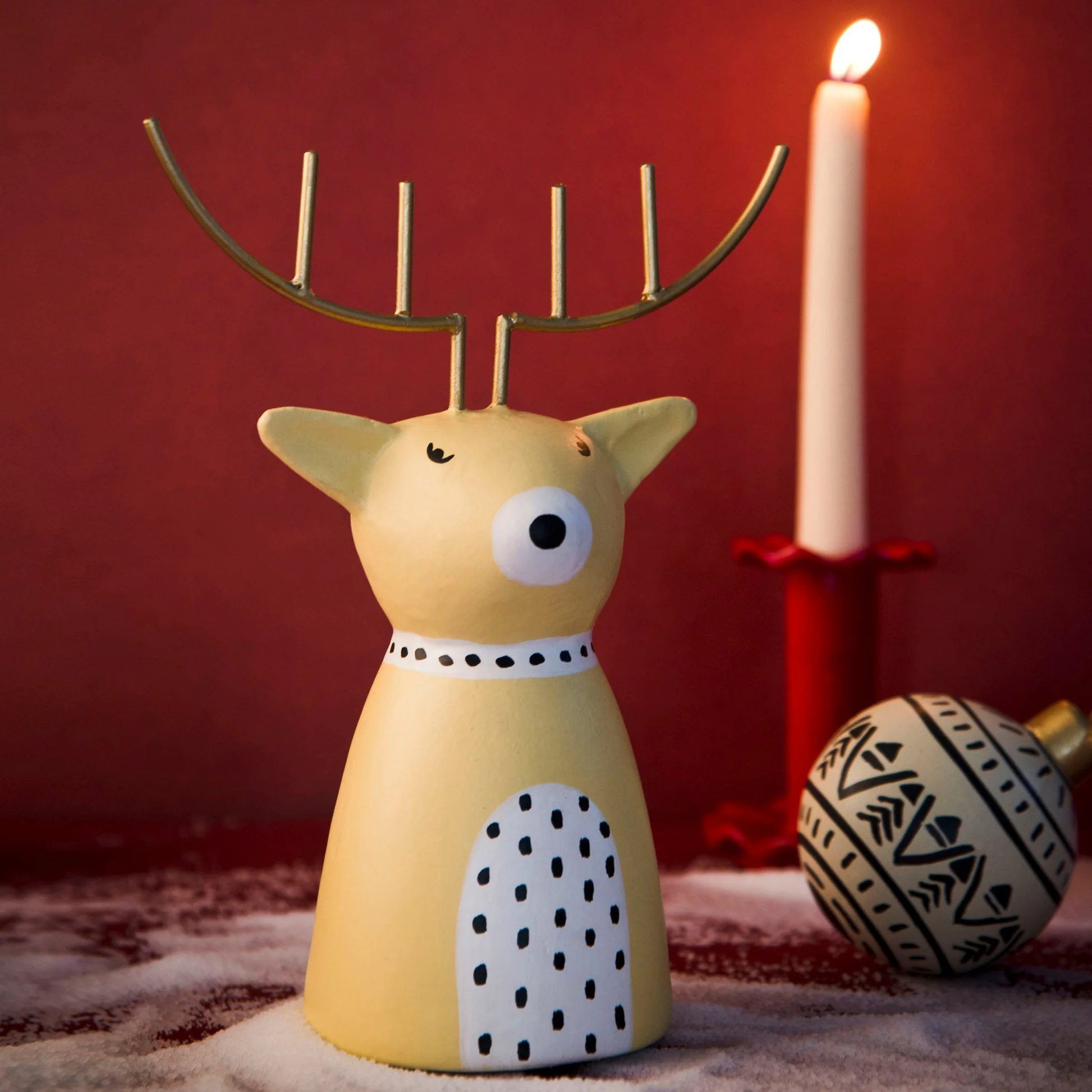 Decorative reindeer figurine with a lit candle on a red background
