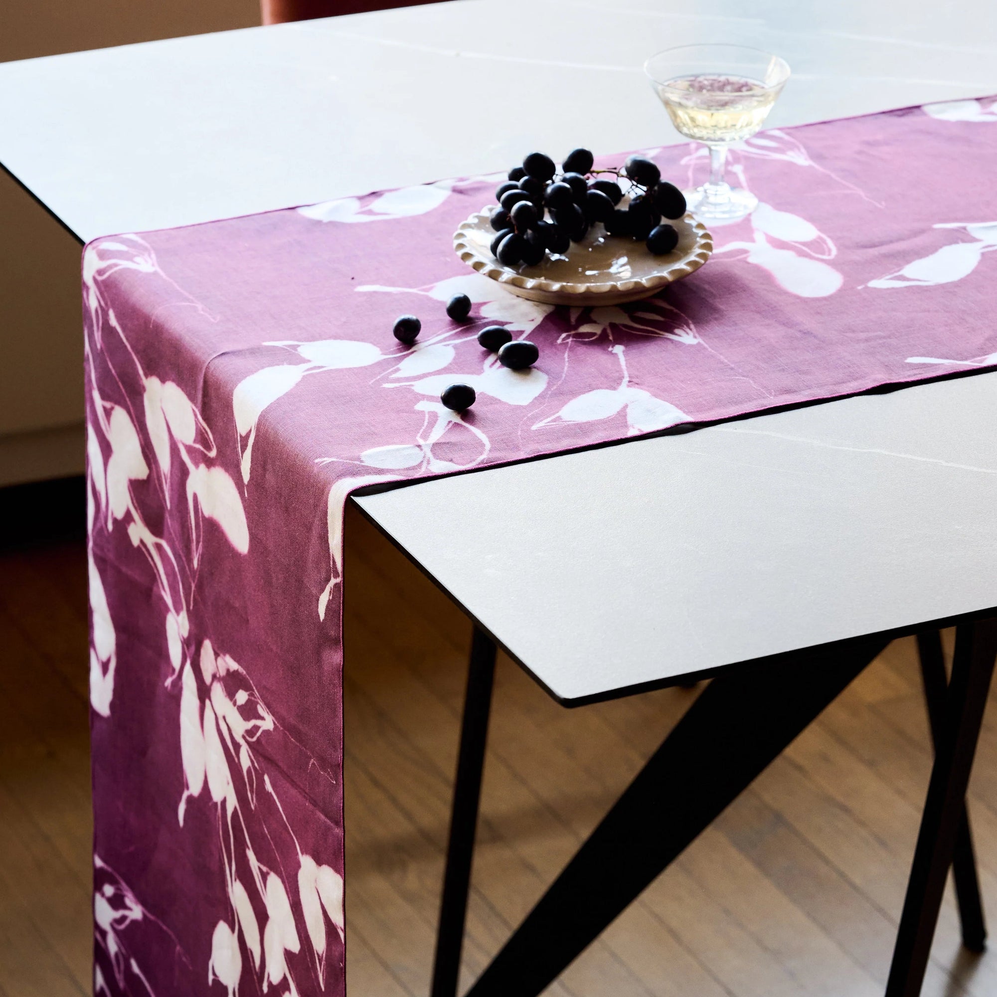 Table with a pink floral tablecloth and blackberries on a white surface.