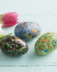 Three decorated Easter eggs with bird and floral patterns on a light blue wooden surface with tulips.