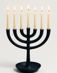 Black menorah with six lit candles on a light gray background