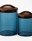 Two blue glass canisters with wooden lids on a white background