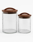 Two glass canisters with wooden lids on a white background