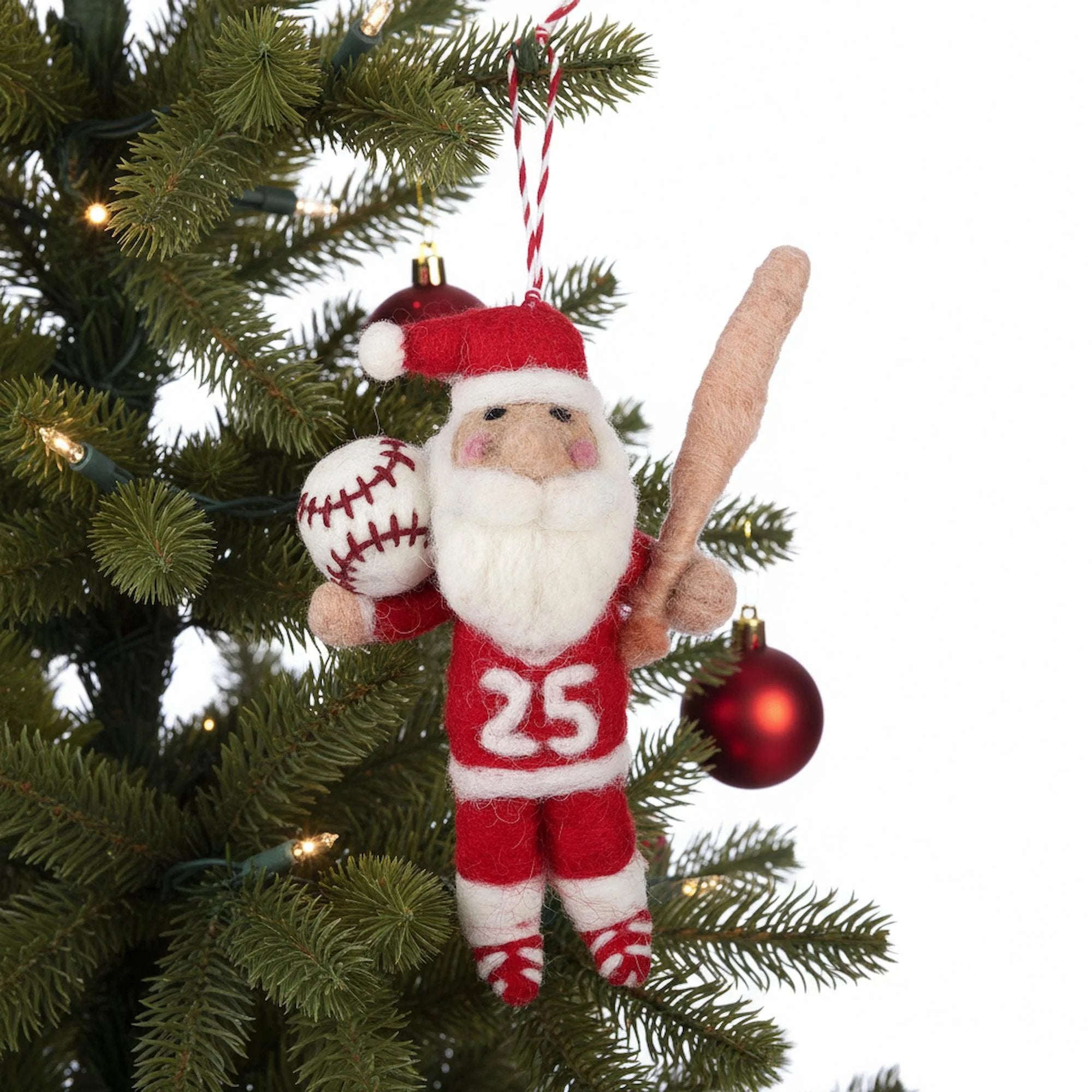 Decorative ornament of a Santa Claus character holding a baseball and bat, hanging on a Christmas tree.