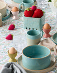 Table setting with ceramic bowls, cups, and decorative eggs on a floral tablecloth.