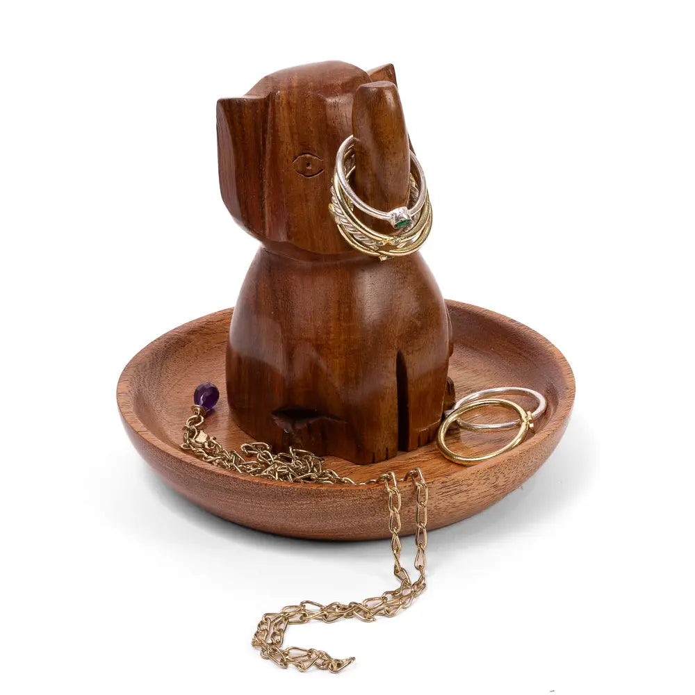 A carved wooden elephant-shaped jewelry stand and tray on a white background, holding gold rings and chains.