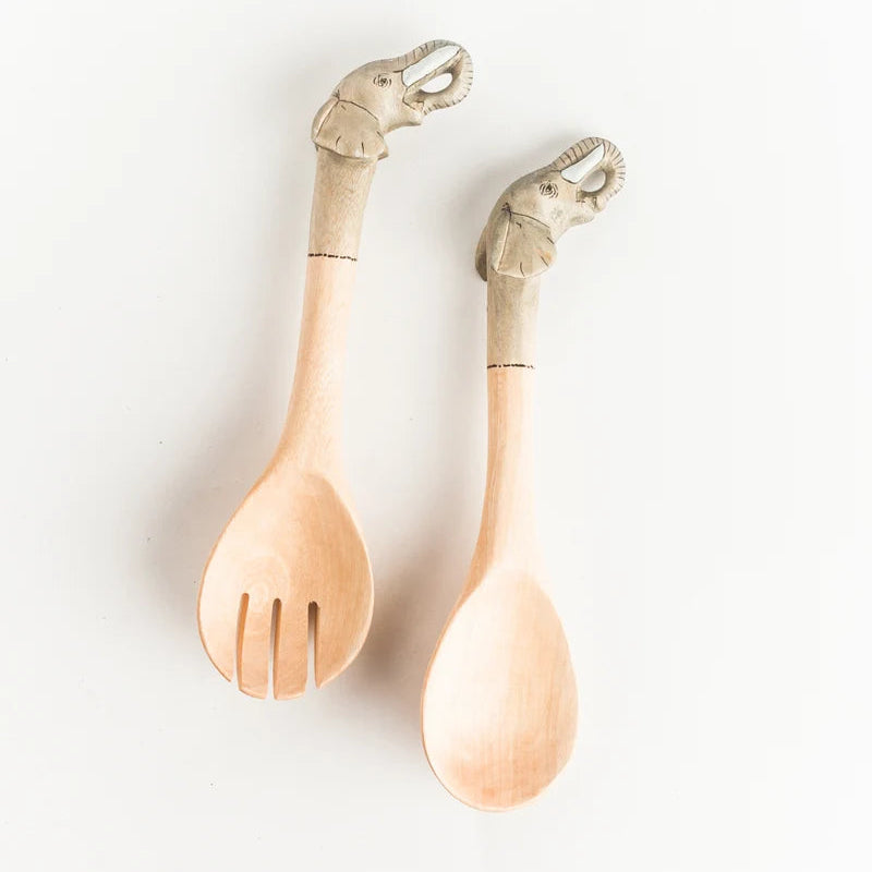 Two light natural wood serving utensils with elephant-shaped handles, one a salad spinner and one a spoon, displayed on a clean white background.