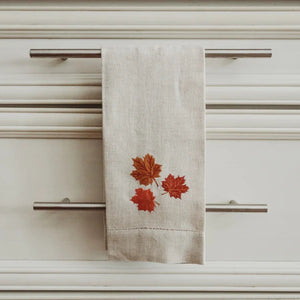 Beige tea towel with red leaf design hanging on a cabinet handle