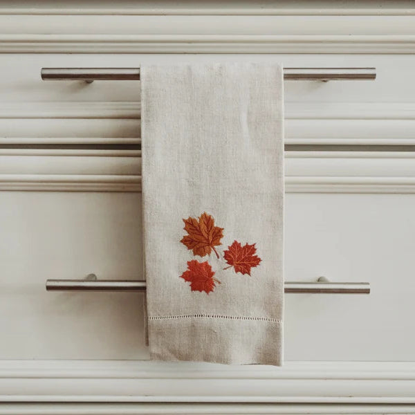 Beige tea towel with red leaf design hanging on a cabinet handle