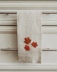 Beige tea towel with red leaf design hanging on a cabinet handle