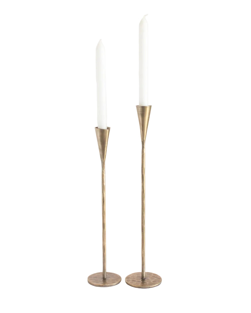 Two tall brass candle holders with white candles on a white background
