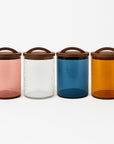 Four colorful glass jars with wooden lids on a white background