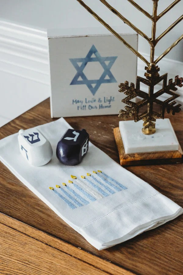 Decorative items including a Menorah, dreidels on a tea towel, and a Star of David card on a wooden surface